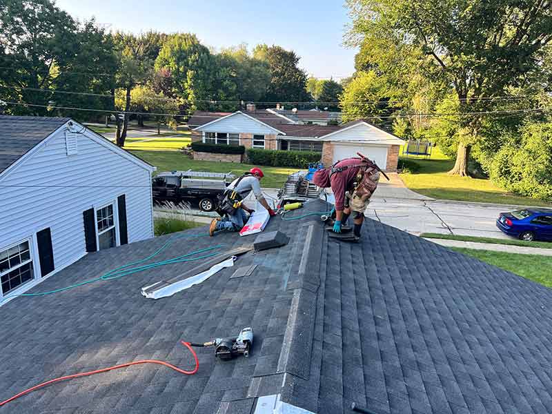 Two Rebel Exteriors Inc. crew members finishing up an install of new GAF dark gray shingles on a residential roof