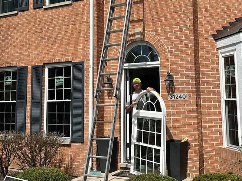 Rebel Exteriors Inc. crew member holding a large window in their hands, getting ready to install it on the second floor of a large, brick home