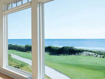 Large floor to ceiling, white Andersen windows overlooking a sidewalk and ocean